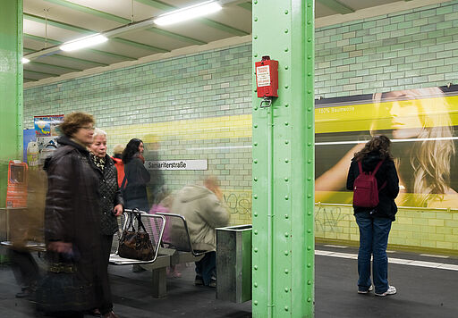 Deutsch – Bildbeschreibung (SEO / Metadaten) Langzeitaufnahme im U-Bahnhof Samariterstraße als Teil des Kunstprojekts „Ey Werbung, was ist los?“. Eine ausfahrende U-Bahn erscheint als bewegte, verschwommene Spur im Vordergrund. Im Hintergrund ist eine beleuchtete Werbetafel mit dem Schriftzug „100 % Baumwolle“ und dem Porträt einer blonden Frau zu sehen. Die Kombination aus Bewegung und statischem Plakat verstärkt die Irritation der werblichen Botschaft im urbanen Transitraum. ⸻ English – Image description (SEO / metadata) Long-exposure view of Samariterstraße underground station in Berlin, part of the art project “Ey Werbung, what’s going on?”. A departing subway train appears as a blurred motion trail in the foreground. In the background, an illuminated advertising panel displays the text “100% cotton” alongside the portrait of a blonde woman. The contrast between movement and the static poster highlights the disruption of advertising logic within the urban transit space.