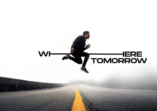 Deutsch (Alt-Text / SEO): Mann springt über eine Straße mit gelbem Mittelstreifen in nebliger Umgebung, typisch amerikanisches Straßenbild. Das Where Tomorrow Is-Logo bewegt sich mit ihm und visualisiert Dynamik, Freiheit und Bewegung. English (Alt text / SEO): Man jumping across a road with a yellow center line in a foggy, distinctly American street setting. The Where Tomorrow Is logo moves along with him, expressing motion, freedom and momentum.