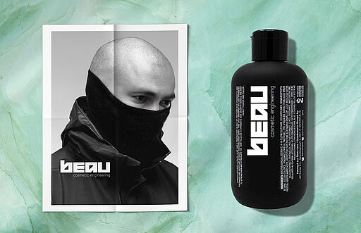 Deutsch (Alt-Text / SEO): Links im Hintergrund ein vermummter asiatischer Mann vor jadegrünem Stein-Hintergrund. Rechts ein Mockup der fiktiven BEAU-Produktverpackung mit cleanem, modernem Premium-Design und Musterstruktur. English (Alt text / SEO): Left in the background, a masked Asian man in front of a jade-green stone backdrop. Right, a mockup of a fictional BEAU product package with clean, modern premium design and a pattern texture concept.
