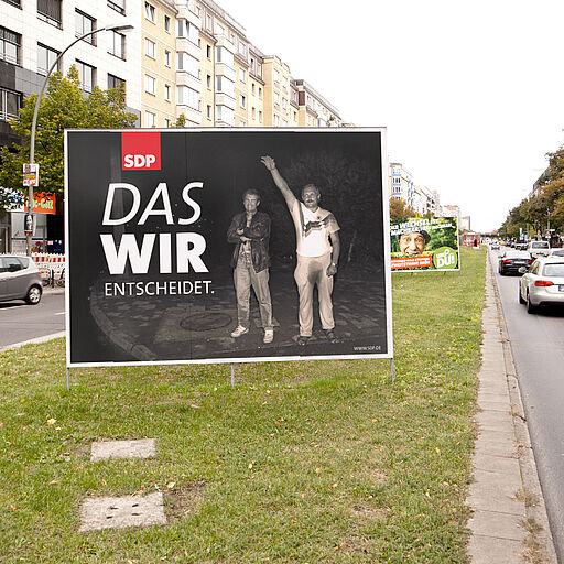 Deutsch – Bildbeschreibung (SEO / Metadaten) Plakatmotiv aus einer Reihe fiktiver Wahlwerbungen im Rahmen eines künstlerischen Designprojekts. Zu sehen ist ein Wahlplakat der Fake-Partei „SDP“ (Anlehnung an bestehende Parteigrafiken) mit dem Slogan „Wir entscheidet“. Im Hintergrund befindet sich ein dokumentarisches Bild der rechtsextremen Ausschreitungen in Rostock-Lichtenhagen (1992), das eine Person mit erhobenem Hitlergruß zeigt. Das Motiv konfrontiert politische Wahlästhetik mit historischer Gewalt und entlarvt die Mechanik politischer Bildsprache durch bewusste Überlagerung. ⸻ English – Image description (SEO / metadata) Poster from a series of fictional election campaigns created as part of an artistic design project. The visual shows a fake political party labeled “SDP,” referencing established party design systems, combined with the slogan “Wir entscheidet.” In the background, a documentary image from the right-wing pogroms in Rostock-Lichtenhagen (1992) is visible, depicting a person performing a Nazi salute. The poster juxtaposes election aesthetics with historical violence, exposing the visual logic of political communication through deliberate contrast.