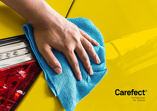 Deutsch (Alt-Text / SEO): Person reinigt ein gelbes Auto mit blauem Mikrofasertuch – CAREFECT Key Visual in Markenfarbe Gelb für wasserfreie, umweltfreundliche Autopflege. English (Alt text / SEO): Person cleaning a yellow car with a blue microfiber cloth – CAREFECT key visual in the brand’s yellow color for waterless, eco-friendly car care.